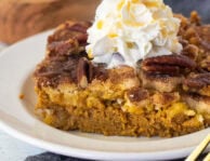 A slice of pumpkin cobbler on a plate with whipped cream and caramel over the top