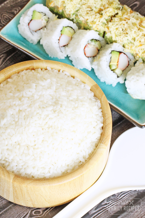Bowl of sushi rice next to two sushi rolls