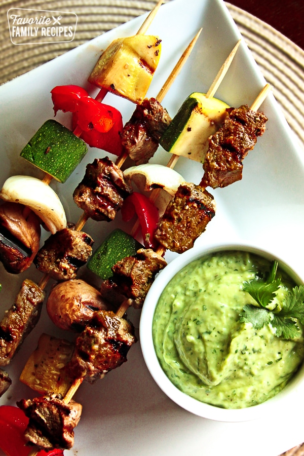 These Steak Kabobs with veggies and Avocado Sauce are slightly spicy, but the cool flavor of the avocado sauce balances it out nicely. Perfect for summer grilling! Steak kabobs on a white plate.