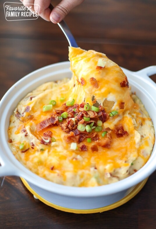 Loaded Mashed Potatoes being spooned out of a baking dish.
