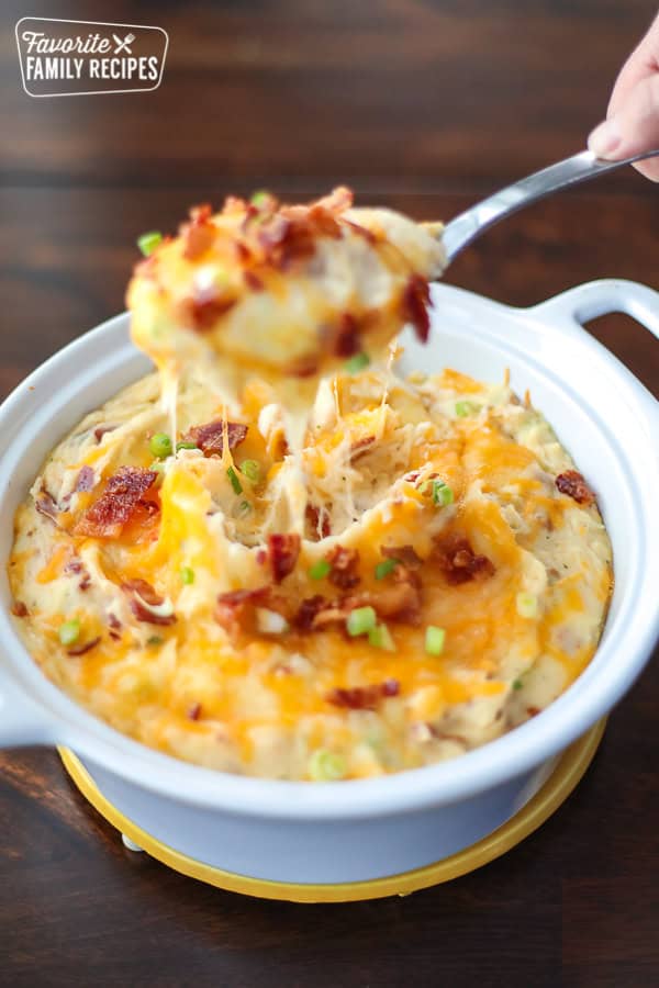 Loaded Mashed Potatoes are a tasty way to use up extra mashed potatoes from holiday meals or Sunday dinner. A cheesy, creamy side to so many meals! Loaded Mashed Potatoes in a white bowl with a spoonful of potatoes pulling away.