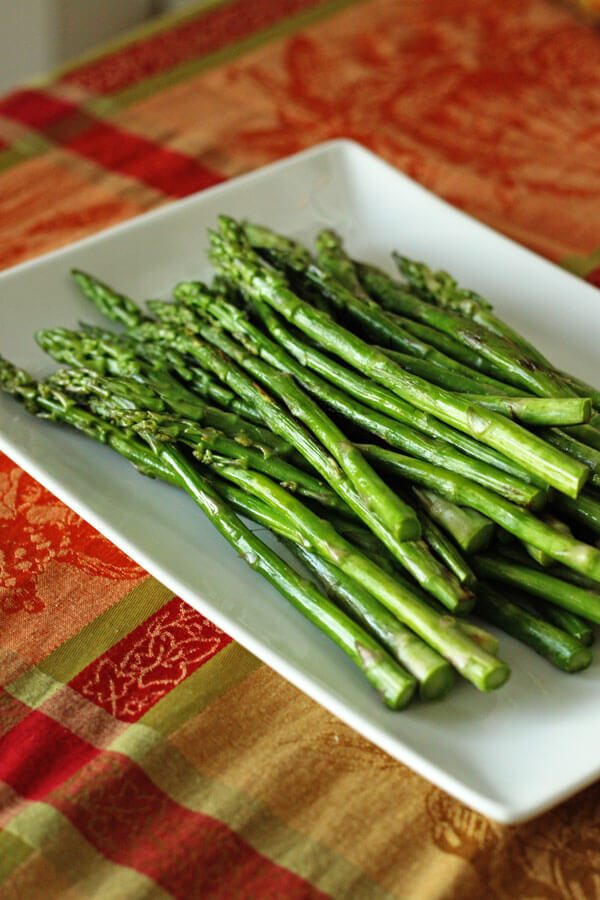 Bright green roasted asparagus on a square white platter.