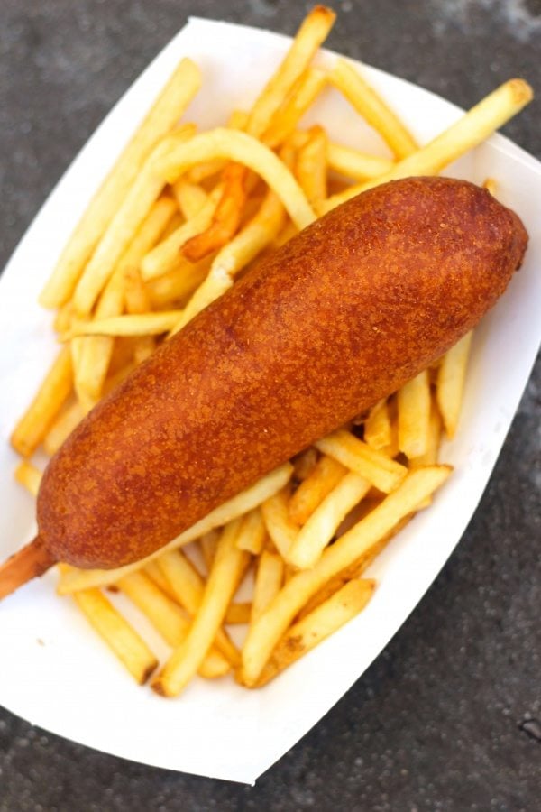 Corn dog with french fries on a white plate.