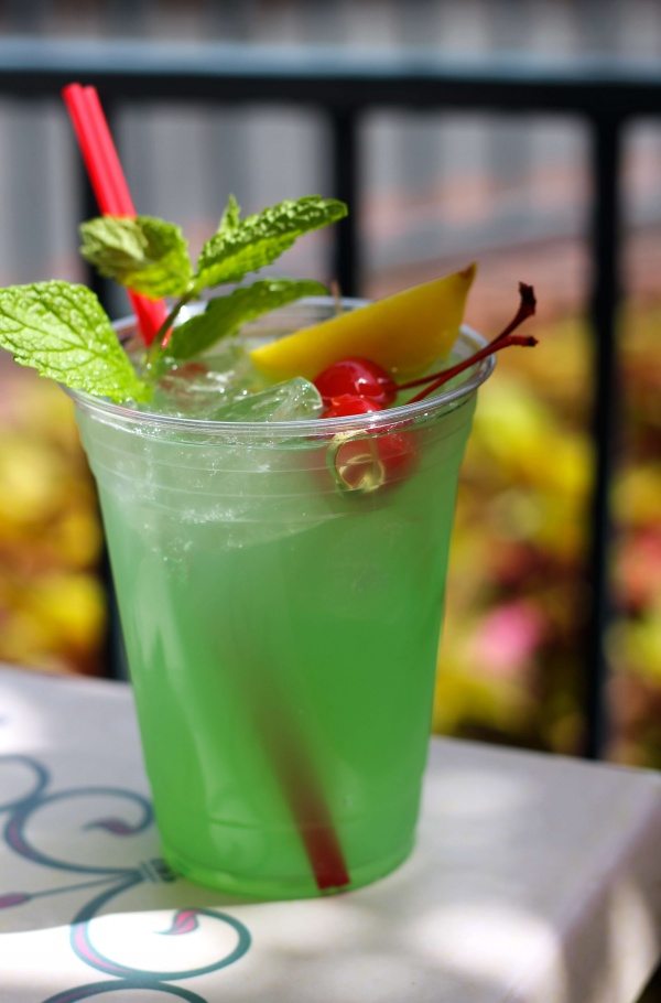 A Disneyland Mint Julep - a green drink garnished with a mint leaf, maraschino cherries, and a lemon slice