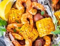 Cajun shrimp foil packets with corn on the cob, red potatoes, and sausage, garnished with parsley and lemon wedges.