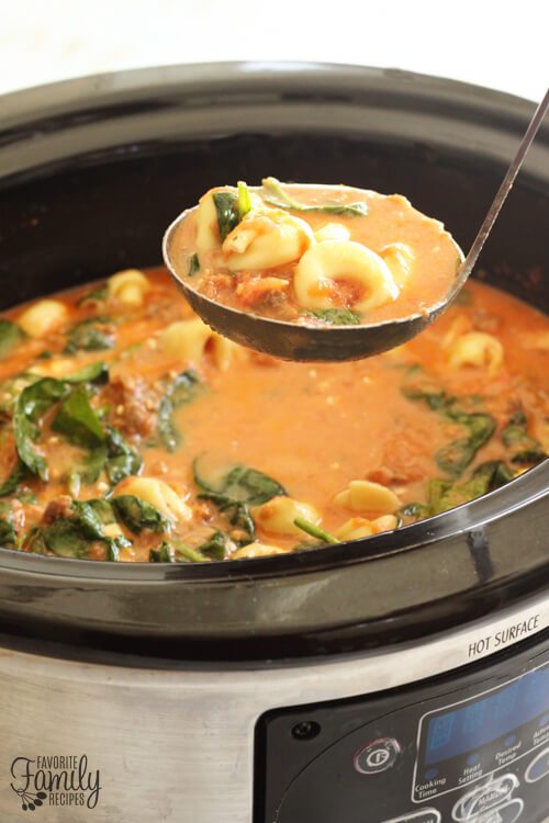 A ladle coming out of a Slow Cooker of Cheese Tortellini Soup 