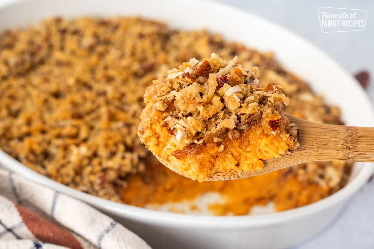 Sweet Potato Casserole with Pecan Topping in a wooden spoon over casserole dish.
