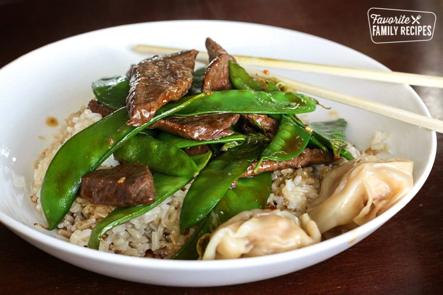 This Beef and Snow Peas is a light and easy recipe! Tender marinated beef and crisp peas go perfectly over rice or noodles for a delicious weeknight supper. Beef and Snow Peas over rice in a large bowl with chopsticks on the side