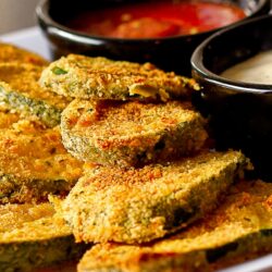 Baked fried zucchini on a white plate with stacked zucchini and marinara sauce.