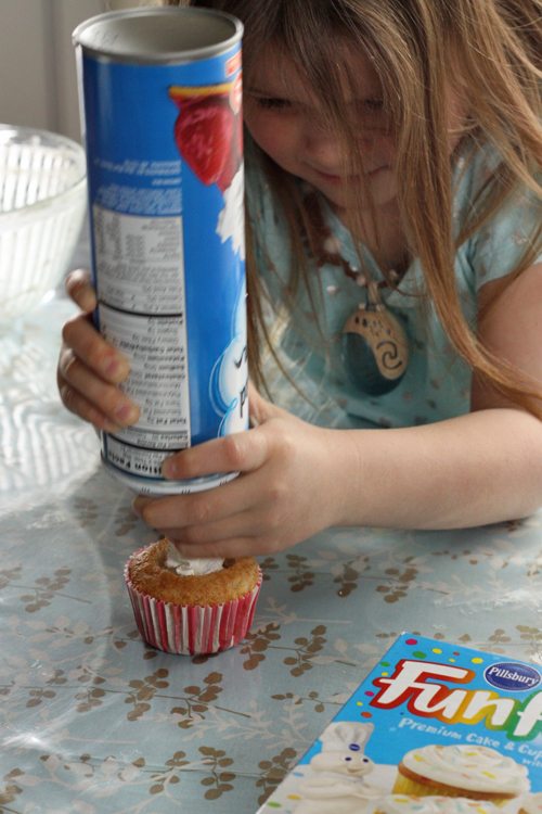 A girl adding whipped cream to the center of a cupcake