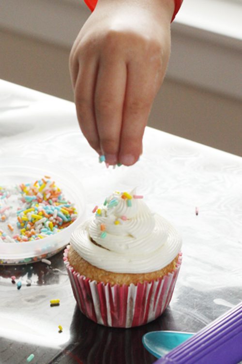 a hand adding sprinkles to a frosted cupcake