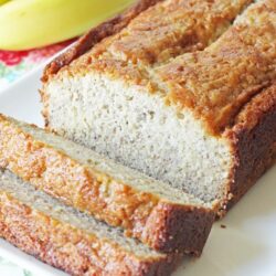 Banana bread slices on a plate with bananas