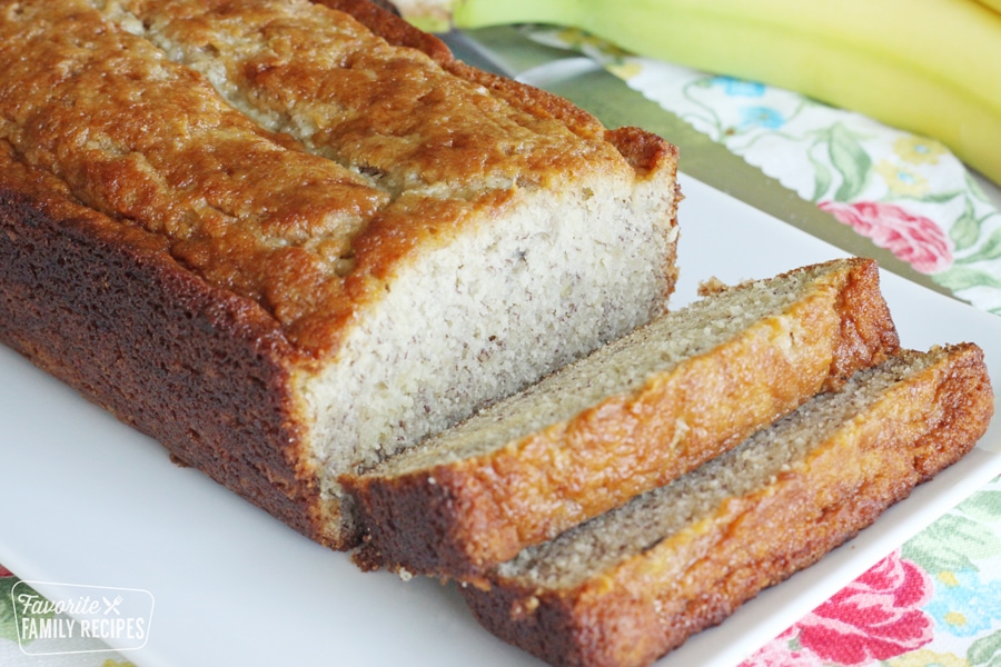 A loaf of banana bread on a white tray sitting on a floral napkin.