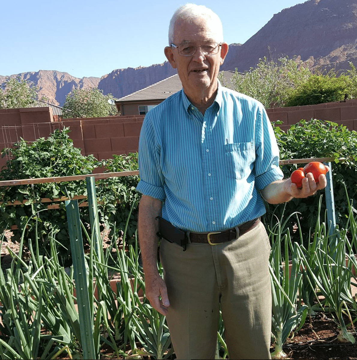 Uncle Larry is in his garden holding fresh garden tomatoes. 