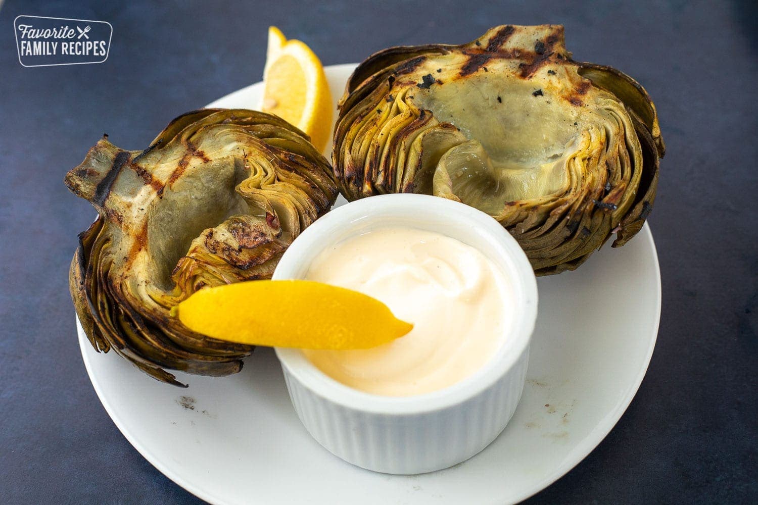 A plate with two grilled artichokes and lemon dip in the center