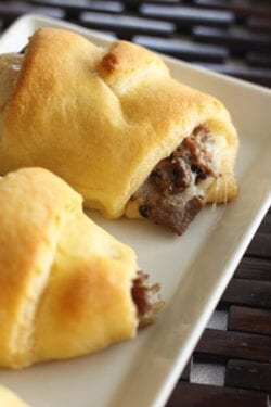 Two cheesesteak crescent rolls on a square white plate