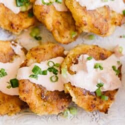 Close up image of cheesy potato cakes drizzled with sauce and sprinkled with green onions