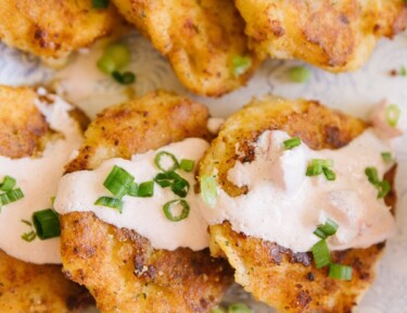 Close up image of cheesy potato cakes drizzled with sauce and sprinkled with green onions