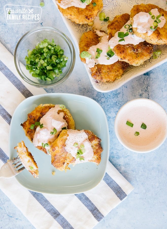 Two Cheesy Potato Cakes on a plate with a platter filled with potato cakes on the side