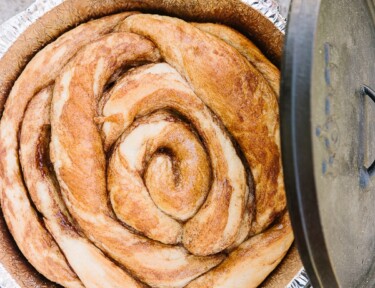 A Cinnamon Roll baked in a Dutch Oven with the Dutch Oven lid on the side