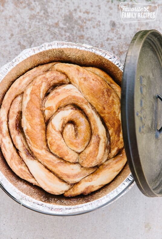 A Cinnamon Roll baked in a Dutch Oven with the Dutch Oven lid on the side
