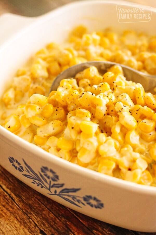 Slow Cooker Creamed Corn in a white casserole dish with a serving spoon scooping out corn