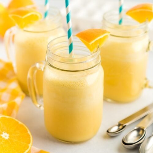 Three mugs of orange julius with blue straws and orange slice garnishes