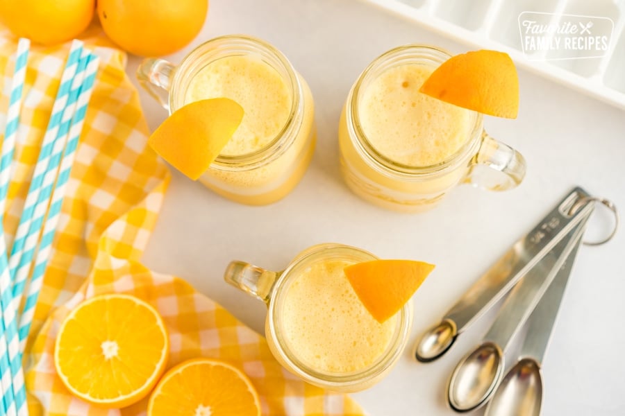We have made this Copycat Orange Julius Recipe since we were kids. It is a refreshing citrusy drink, perfect for a warm summer day! Mugs of orange Julius with orange slices as garnishes.