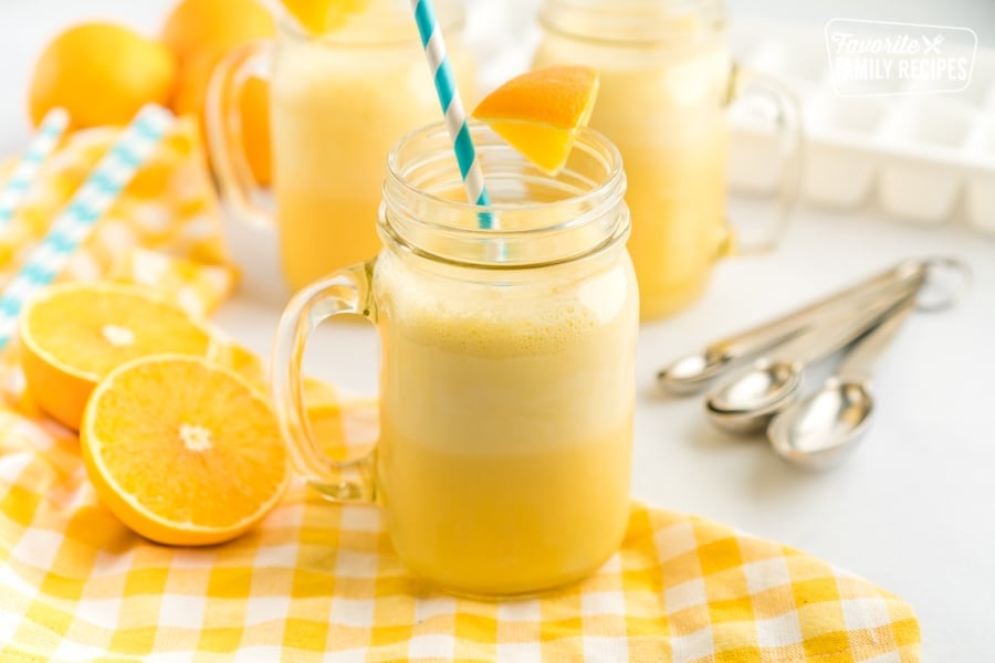 A mug of Orange Julius with a blue straw and an orange slice garnish.