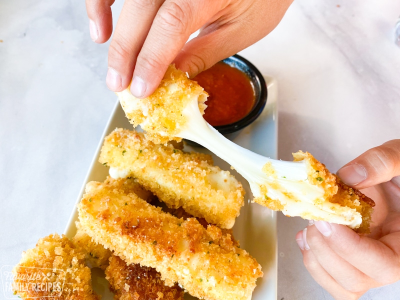 Mozzarella stick being pulled apart to show long string of cheese