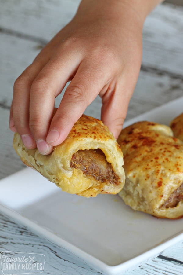 A child's hand picking up a cooked Australian Sausage Roll