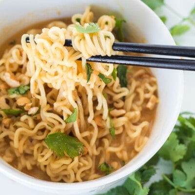 Peanut butter ramen in a white bowl with chopsticks pulling the ramen out of the bowl.