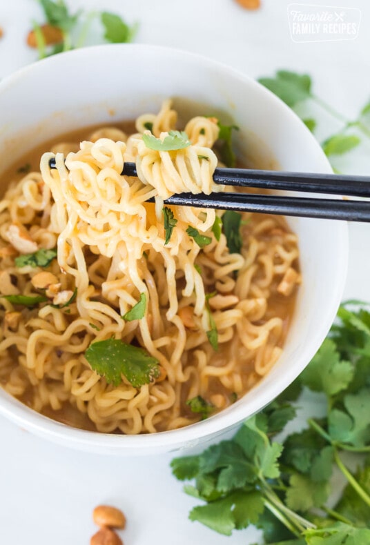 Peanut butter ramen in a white bowl with chopsticks pulling the ramen out of the bowl.