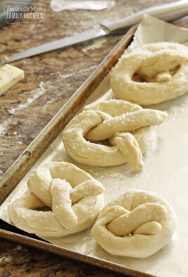 Four uncooked pretzels on a baking sheet.