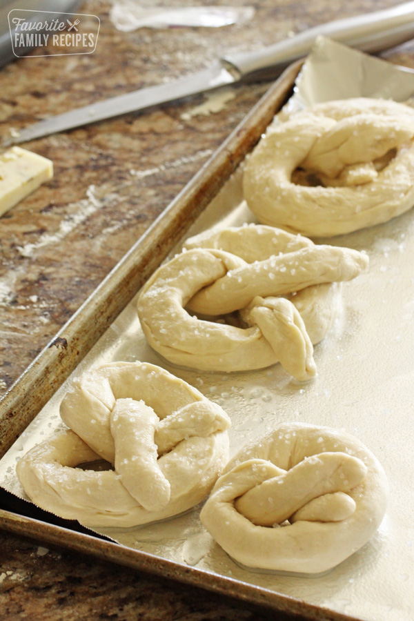 Four uncooked pretzels on a baking sheet