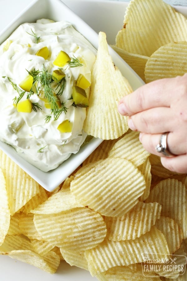 Potato chip being dipped in creamy dill pickle dip