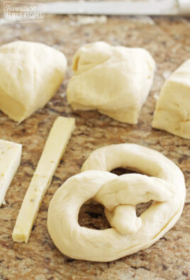 Soft pretzel shaped before baking with stick of cheese and uncooked dough.