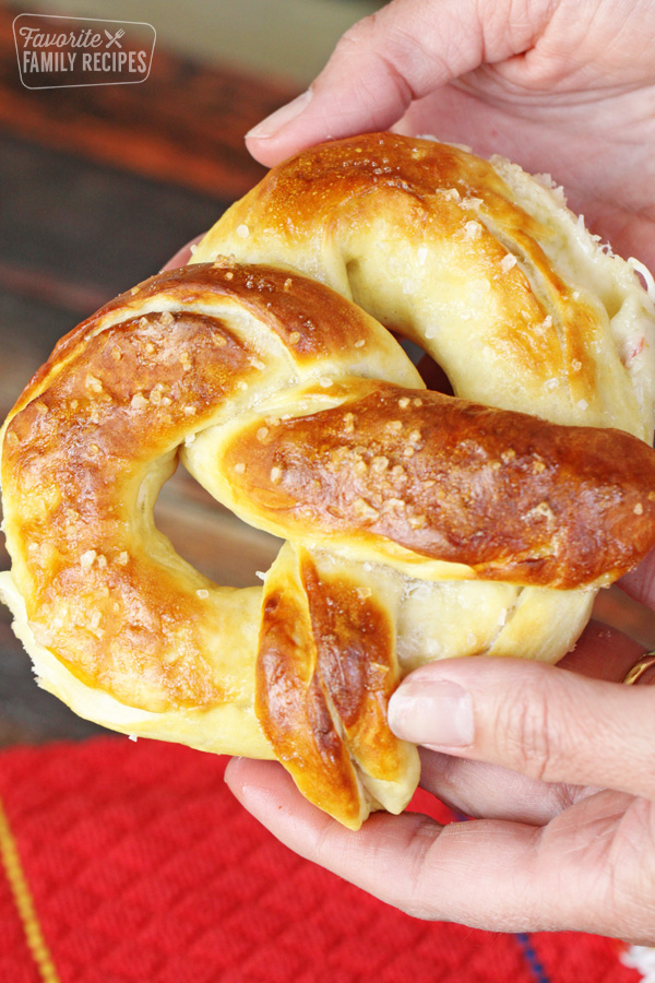 Large, whole soft pretzel being held above a table