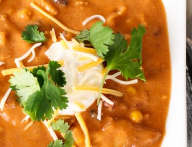A bowl of Instant Pot Chicken Enchilada soup garnished with sour cream, shredded cheese, and cilantro