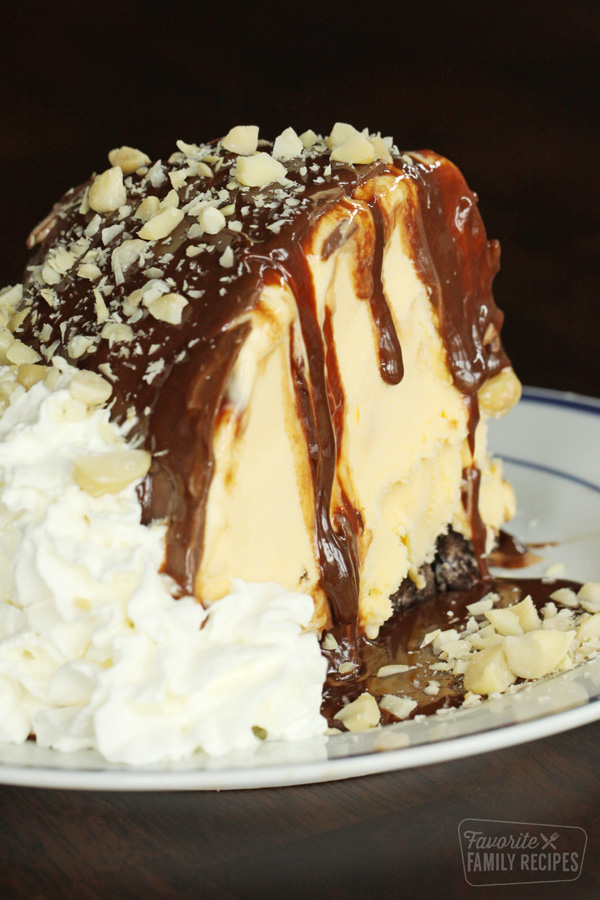 A large slice of hula pie with fudge dripping from the sides with whipped cream and chopped macadamia nuts