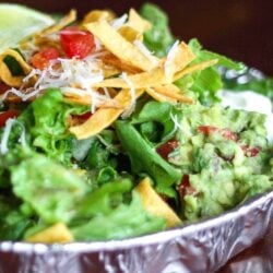 Copycat Cafe Rio Sweet Pork Salad with chopped lettuce, shredded pork, cilantro rice, black beans, guacamole, pico de gallo, and tortilla strips served in an aluminum tin