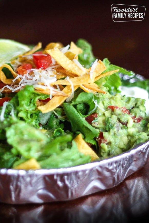 Copycat Cafe Rio Sweet Pork Salad with chopped lettuce, shredded pork, cilantro rice, black beans, guacamole, pico de gallo, and tortilla strips served in an aluminum tin