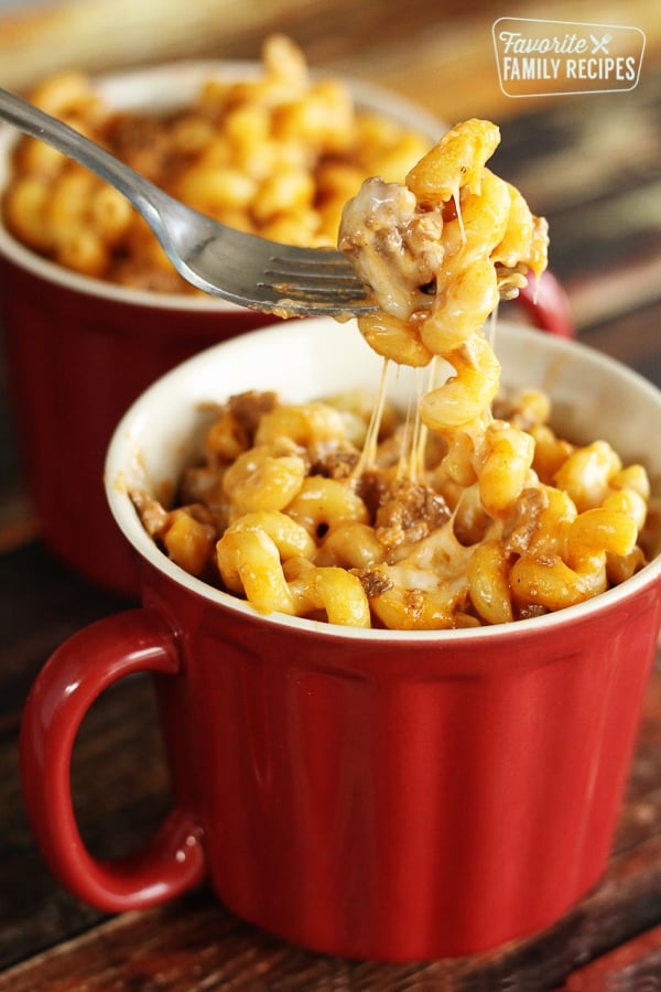 15 Minute Beef and Noodle Skillet is shown in a red mug and a fork is lifting some of the cheesy pasta above it.