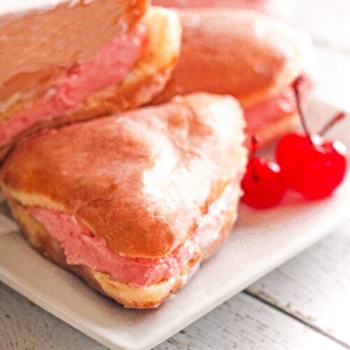 3 alligator jaw pastries with marischino cherries on a white plate.