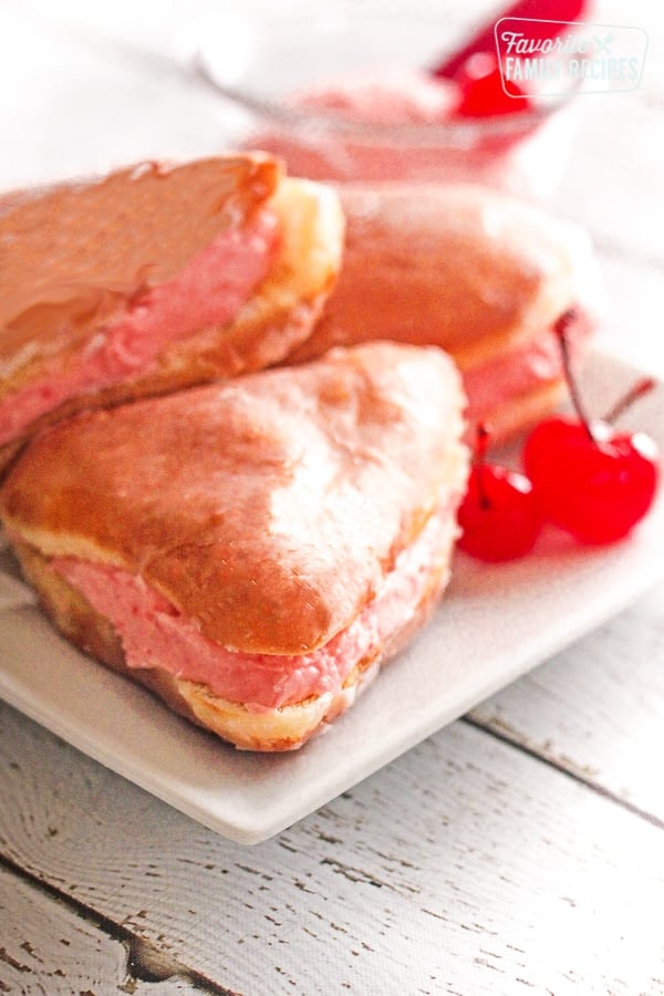 3 alligator jaw pastries with marischino cherries on a white plate.