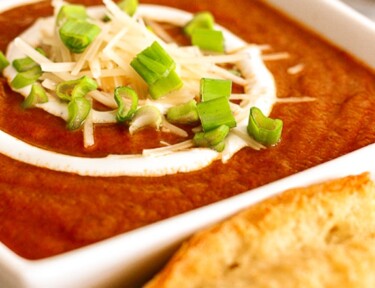 Cafe Zupas Tomato Basil Soup with sour cream, cheese, and green onions in a white bowl