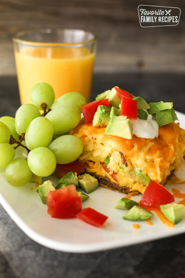 California Breakfast Casserole served on a white plate topped with chopped tomatoes and avocado with green grapes and orange juice on the side