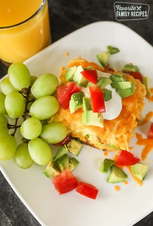 A slice of California Breakfast Casserole served with a bunch of green grapes and a glass of orange juice