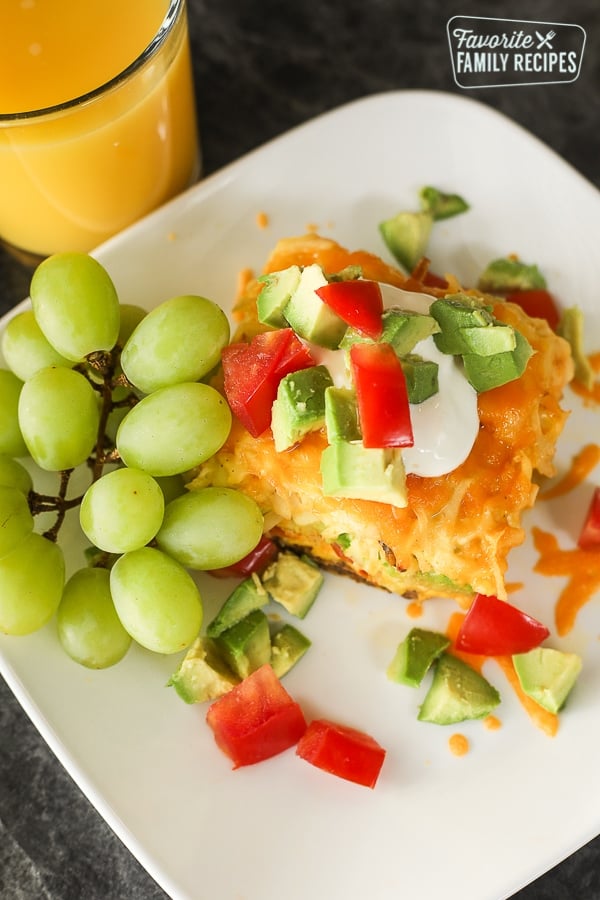 A slice of California Breakfast Casserole served with a bunch of green grapes and a glass of orange juice