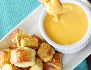 Golden pretzel bites being dipped in cheese